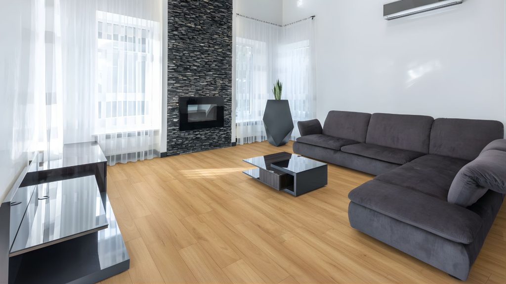 Modern Perth living room with light timber-look laminate flooring, grey sofa and stone fireplace showcasing a clean, stylish laminate floor finish.